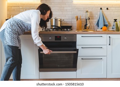 young pretty woman open oven to cook. domestic kitchen concept. copy space