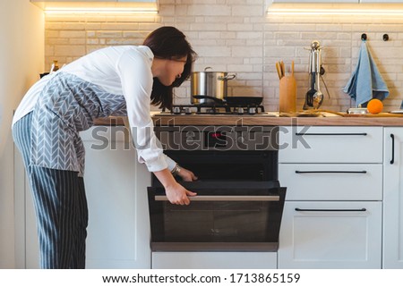 young pretty woman open oven to cook. domestic kitchen concept