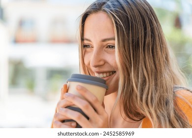 Young pretty woman at outdoors holding a take away coffee with happy expression