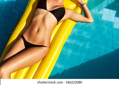 Jovem bonita mulher com corpo bronzeado perfeito deitado no colchão de ar amarelo na piscina no verão e se divertir