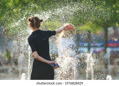 Young pretty woman playing with cold water of city  fountains. Hot spring day in the big city. Fresh water splashes. Youth having fun. Leisure carefree time concept. Back, rear view.