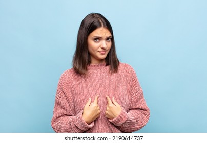 Young Pretty Woman Pointing To Self With A Confused And Quizzical Look, Shocked And Surprised To Be Chosen