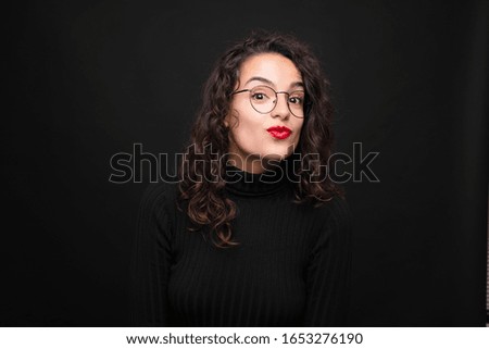 young pretty woman pressing lips together with a cute, fun, happy, lovely expression, sending a kiss against black background.