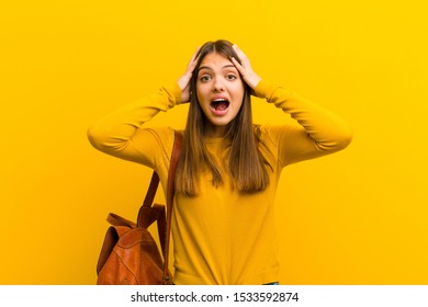 young pretty woman raising hands to head, open-mouthed, feeling extremely lucky, surprised, excited and happy against orange background - Shutterstock ID 1533592874