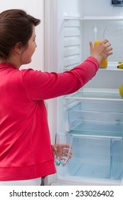 Young Pretty Woman Reaching For Orange Juice In The Fridge