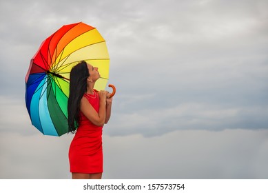 Young pretty woman in red dress with rainbow umbrella against overcast sky