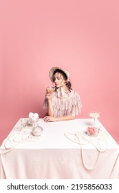 Young Pretty Woman With Retro Style Hairdo In Bonnet And Vintage Dress Sitting At Holiday Table Isolated On Pink Background. Eras Comparison, Art, Beauty Holiday, Fashion, Emotions, And Ad