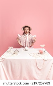 Young Pretty Woman With Retro Style Hairdo In Bonnet And Vintage Dress Sitting At Holiday Table Isolated On Pink Background. Eras Comparison, Art, Beauty Holiday, Fashion, Emotions, And Ad