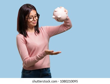 Young Pretty Woman Sad And Disappointed, Holding A Piglet Bank, No Money Left, Trying To Get Something Out, Face Of Anger And Anguish, Concept Of Poverty