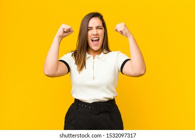 young pretty woman shouting aggressively with an angry expression or with fists clenched celebrating success isolated against orange wall - Shutterstock ID 1532097317
