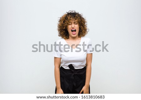 young pretty woman shouting aggressively, looking very angry, frustrated, outraged or annoyed, screaming no against white wall