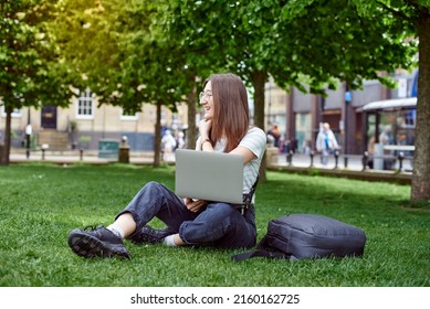 A young pretty woman sits on the lawn with a laptop. The girl works remotely on a laptop in the fresh air. The concept of remote work. - Shutterstock ID 2160162725
