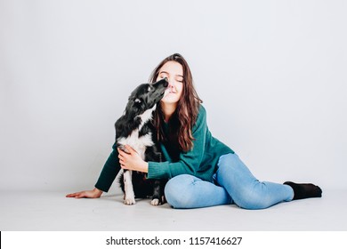 Young Pretty Woman Sits Together With Her Border Collie Dog And Hugs It Isolated On White Background. Dog Licks Owner. Studio Portrait.