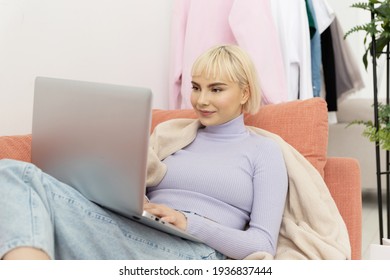 Young Pretty Woman Sitting At Home And Working Remotely Behind A Laptop Lying On The Couch