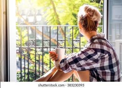 Young pretty woman  sitting at opened window drinking coffee and looking outside enjoys of rest. Dream