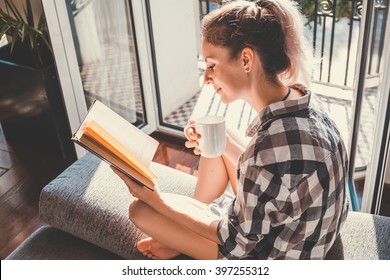 Young pretty woman  sitting at opened window drinking coffee and reading a book enjoys of rest