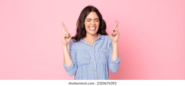 young pretty woman smiling and anxiously crossing both fingers, feeling worried and wishing or hoping for good luck - Shutterstock ID 2320676393