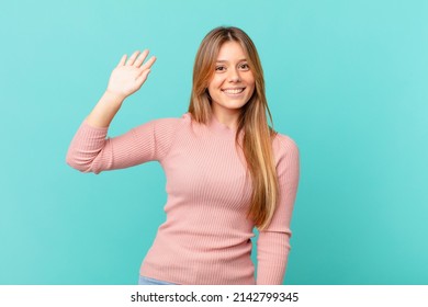 young pretty woman smiling happily, waving hand, welcoming and greeting you