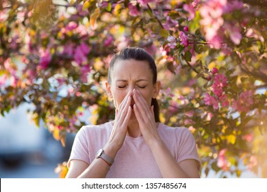 Young pretty woman sneezing in front of blooming tree. Spring allergy concept - Shutterstock ID 1357485674