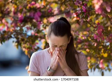 Young Pretty Woman Sneezing In Front Of Blooming Tree. Spring Allergy Concept