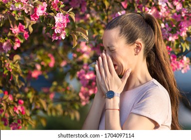 Young Pretty Woman Sneezing In Front Of Blooming Tree. Spring Allergy Concept