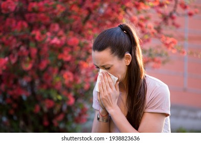 Young pretty woman sneezing in front of blooming tree. Spring allergy concept