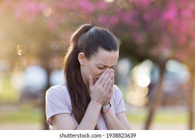 Young Pretty Woman Sneezing In Front Of Blooming Tree. Spring Allergy Concept