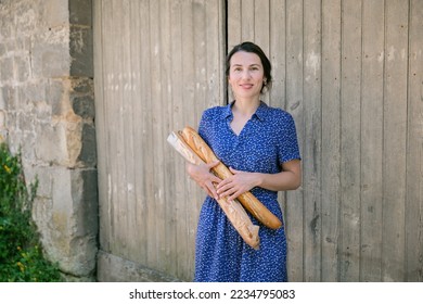 Joven linda mujer parada con baguettes francesas en sus manos en el campo