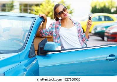Young pretty woman in sunglasses standing near convertible with keys in hand - concept of buying a used car or a rental car