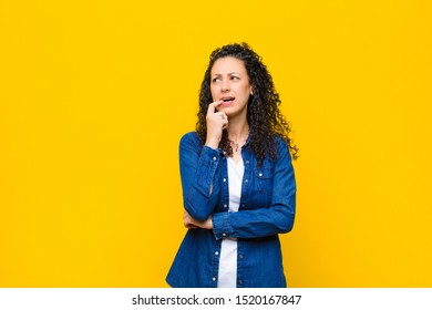 young pretty woman with surprised, nervous, worried or frightened look, looking to the side towards copy space against orange wall - Shutterstock ID 1520167847