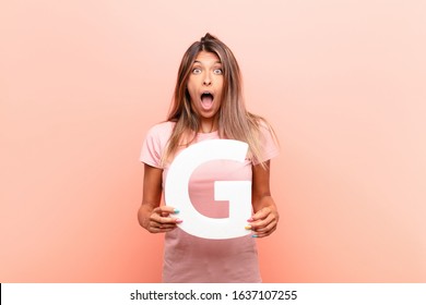 young pretty woman surprised, shocked, amazed, holding the letter G of the alphabet to form a word or a sentence.