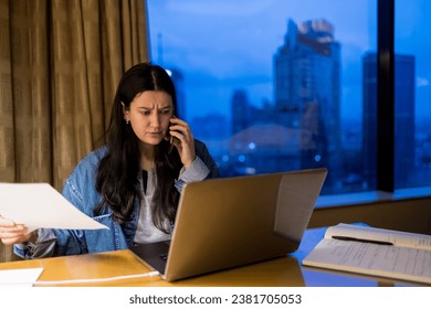 Young pretty woman using laptop and mobile phone in penthouse or luxury hotel room doing paper work report. Businesswoman in skyscraper apartment against night city background working late at nigh. - Powered by Shutterstock