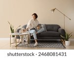 Young pretty woman using tablet and drinking coffee on sofa in light living room