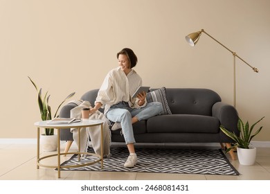 Young pretty woman using tablet and drinking coffee on sofa in light living room - Powered by Shutterstock