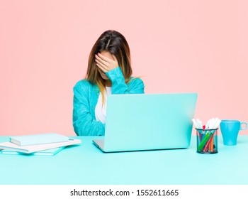 young pretty woman working with a laptop looking stressed, ashamed or upset, with a headache, covering face with hand