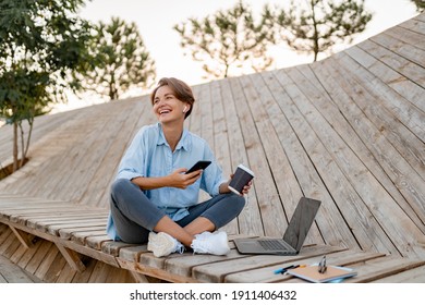 Young Pretty Woman Working On Laptop In IT Outside In Modern Park Street Sitting On Remote Work, Summer Style Casual Smiling Talking On Wireless Earpods Drinking Coffee