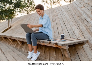 Young Pretty Woman Working On Laptop In IT Outside In Modern Park Street Sitting On Remote Work, Summer Style Casual Smiling Talking On Wireless Earpods Drinking Coffee