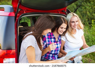 Young pretty women friends travel by car. Summer holidays and active recreation. Positive emotions from the adventure. The girls are looking at the map - Powered by Shutterstock