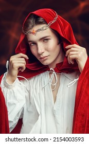 A Young Prince Of Elves In A Red Velvet Cloak And A Crown On His Head. Studio Portrait On A Black Background. Fairy Tale, Magic. Fantasy.