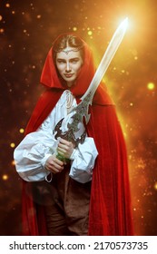 A young prince of elves in a red velvet cloak and a crown stands with a shining sword in his hands. Studio shot on a black background with lights. Fairy tale, magic. Fantasy. - Shutterstock ID 2170573735