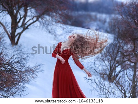 A young princess dances in the wind, her long hair is beautifully fluttering. Pose is light and airy, a sense of freedom femininity relax. Lady in a red dress. Art photography. Winter frozen landscape