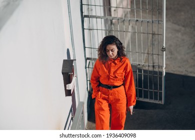 Young Prisoner Woman In Orange Suit At Jail Smoking. Female In Colorful Overalls Portrait.