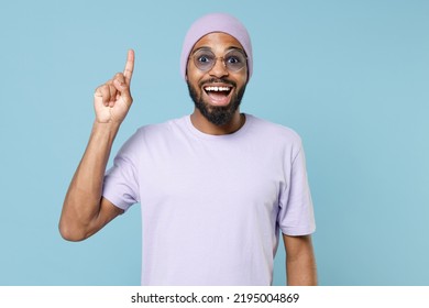 Young Proactive Insighted Unshaven Student Black African Man 20s In Violet T-shirt Hat Glasses Insighted Holding Index Finger Up With Great New Idea Isolated On Pastel Blue Background Studio Portrait