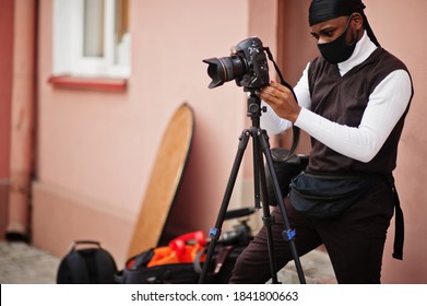 Young professional african american videographer holding professional camera with pro equipment. Afro cameraman wearing black duraq and face protect mask, making a videos.