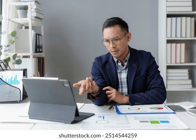 Young professional is analyzing data on his tablet and having a video call in his office, showing a concerned expression as he reviews important information - Powered by Shutterstock