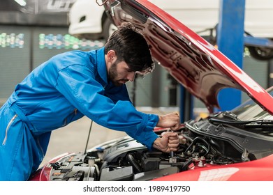 Young Professional Automobile Engine Repair Technician Inspecting Car Engine And Lubricant System By Using Check List In Modern Car Service Shop. Automotive Business Or Car Repair Concept.