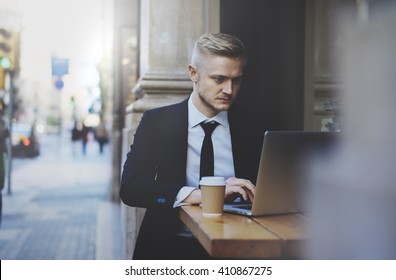 Young Professional Businessman Wearing Suit And Using Modern Laptop Outdoors, Successful Manager Working In Cafe During Break And Searching Information In Internet On His Portable Computer