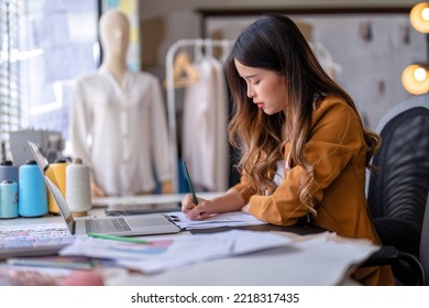Young professional clothes fashion designer sitting near sewing machine use laptop computer   tablet pc to reference   draw the design the paper pattern