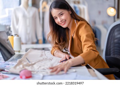 Young professional clothes fashion designer sitting near sewing machine use laptop computer   tablet pc to reference design smiling portrait to camera