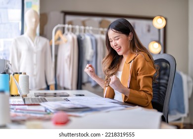 Young professional clothes fashion designer sitting near sewing machine use laptop computer   tablet pc to reference   she got the good news as world winner clothes designer